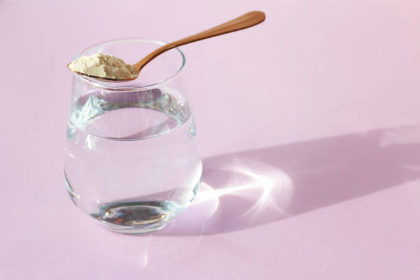 Glass of water with a spoonful of powder on purple background